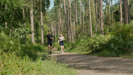 Pareja-De-Mediana-Edad-Haciendo-Ejercicio-Al-Aire-Libre-Corriendo-Por-Una-Pista-A-Través-Del-Bosque-Hacia-La-Cámara-Vistiendo-Ropa-Deportiva-Filmada-En-Tiempo-Real